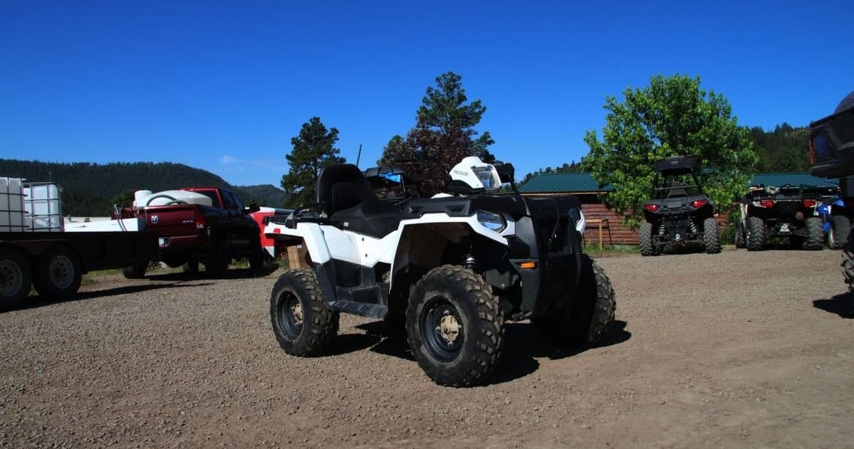 White ATV parked on dirt lot with pine forest mountain backdrop