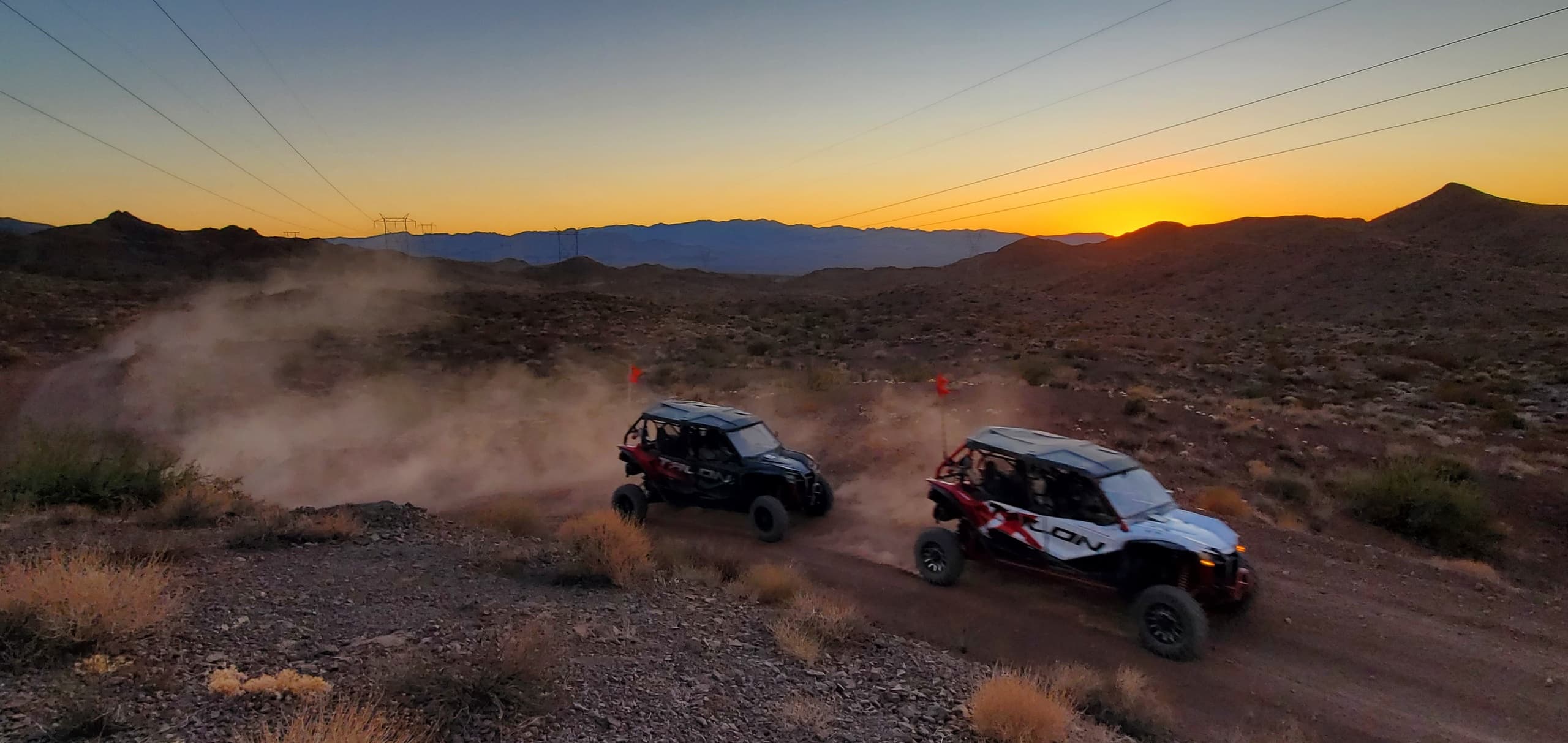 UTVs racing across desert at sunset kicking up dust trails
