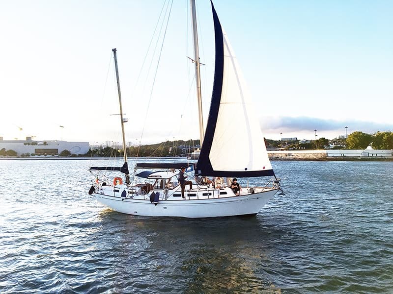 White sailboat near harbor waters with crew aboard, daylight
