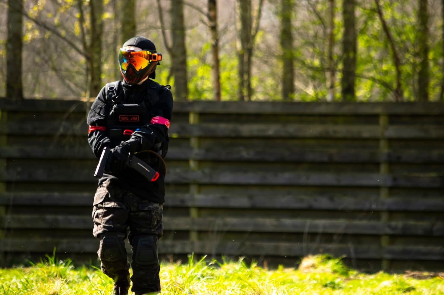 Airsoft player standing by wooden barricade in sunlit forest