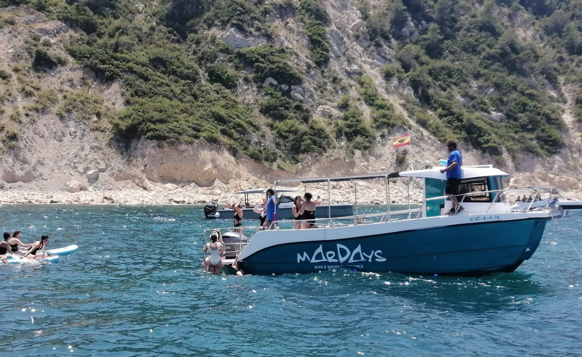 Tour boat anchored near rocky coastline with swimmers and divers
