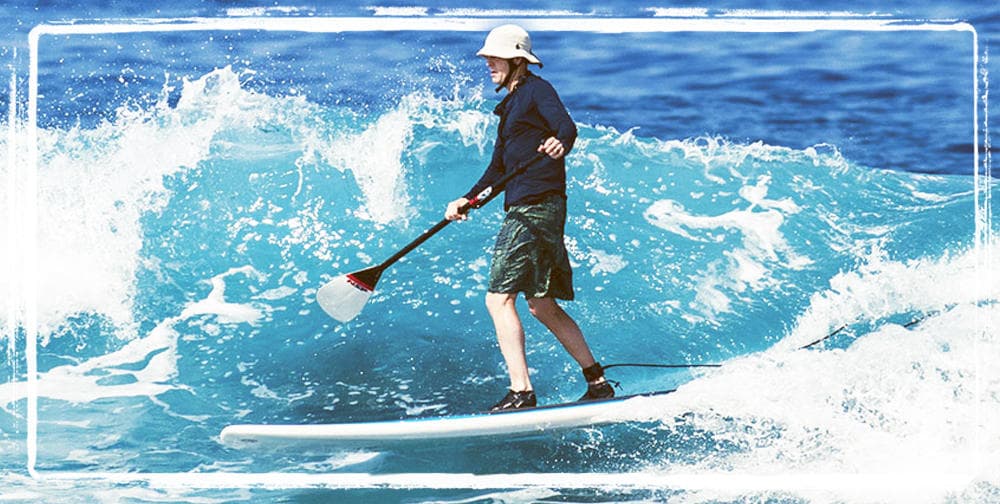 Paddleboarder riding an ocean wave near rocky Kona shoreline