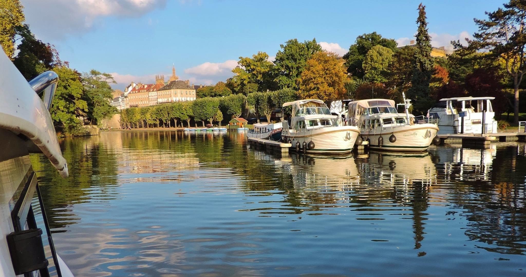 Boats moored in marina on tranquil river under blue sky