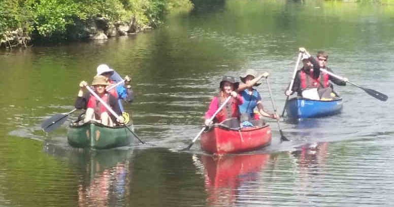 Group canoeing on calm river with green banks, paddling together