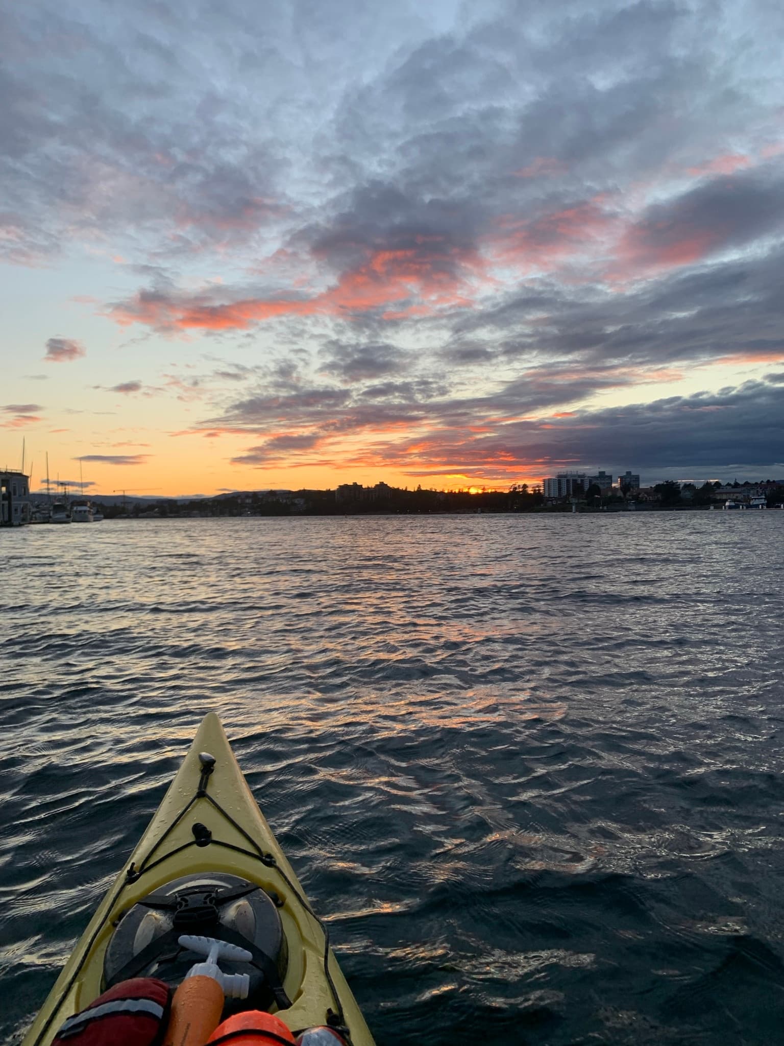 Bow of kayak heading toward harbor sunset over calm ocean