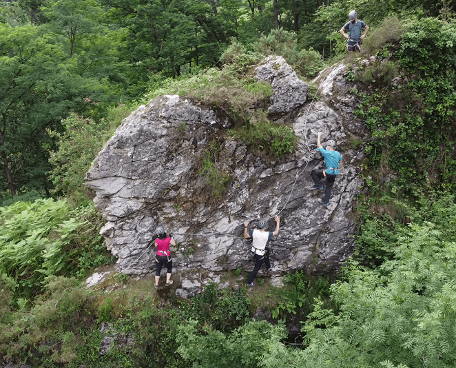Group scrambling up a rocky cliff in lush green forest terrain