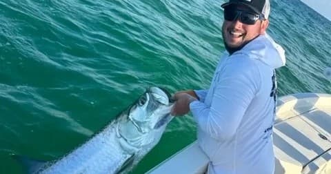 Angler reeling and holding large tarpon from open ocean boat