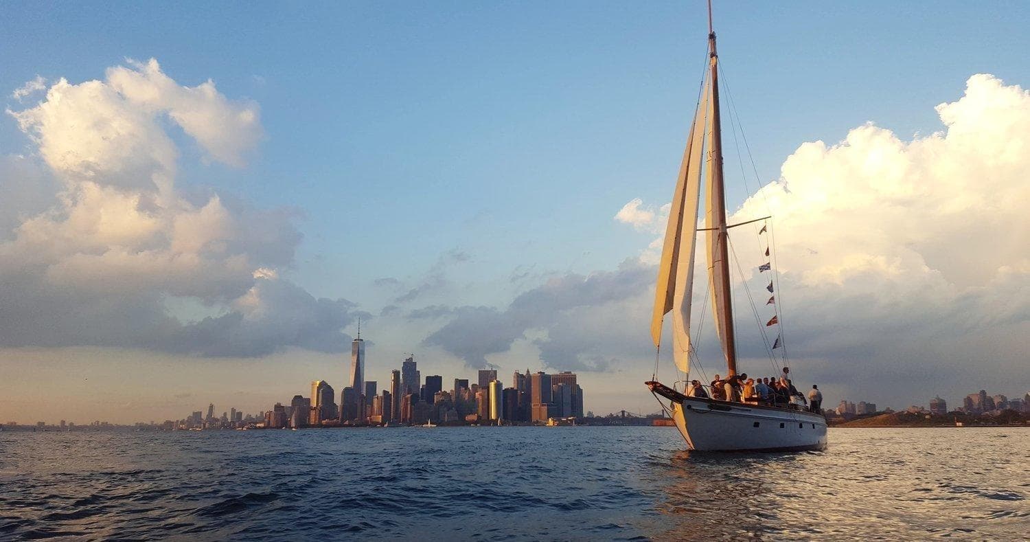 Sailboat cruising near New York City skyline at sunset