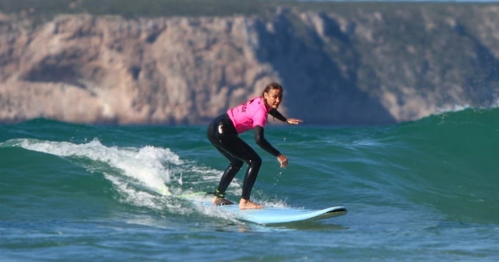 Surfer riding green wave with coastal cliffs in background