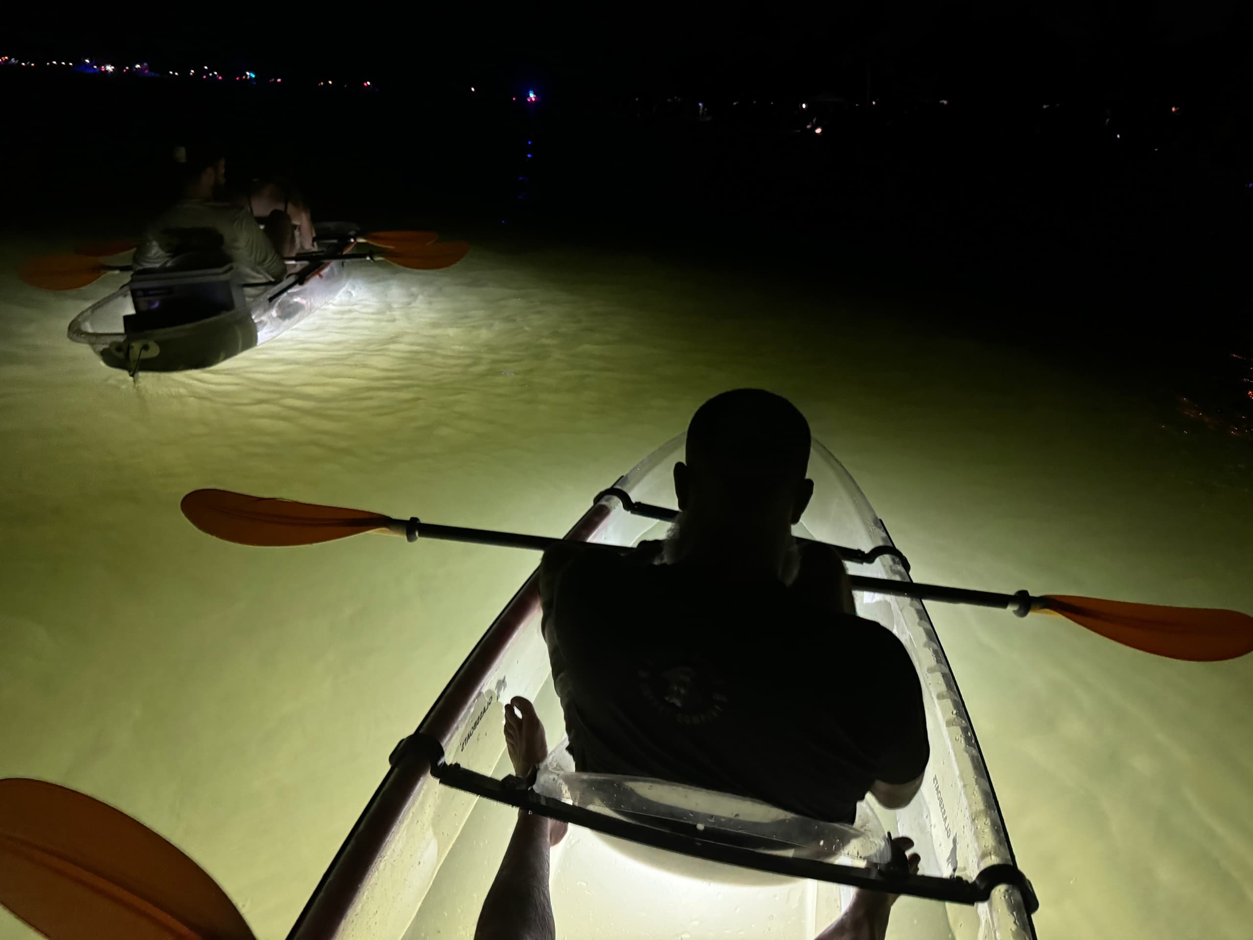 Night illuminated clear kayak tour paddling over shallow bioluminescent water