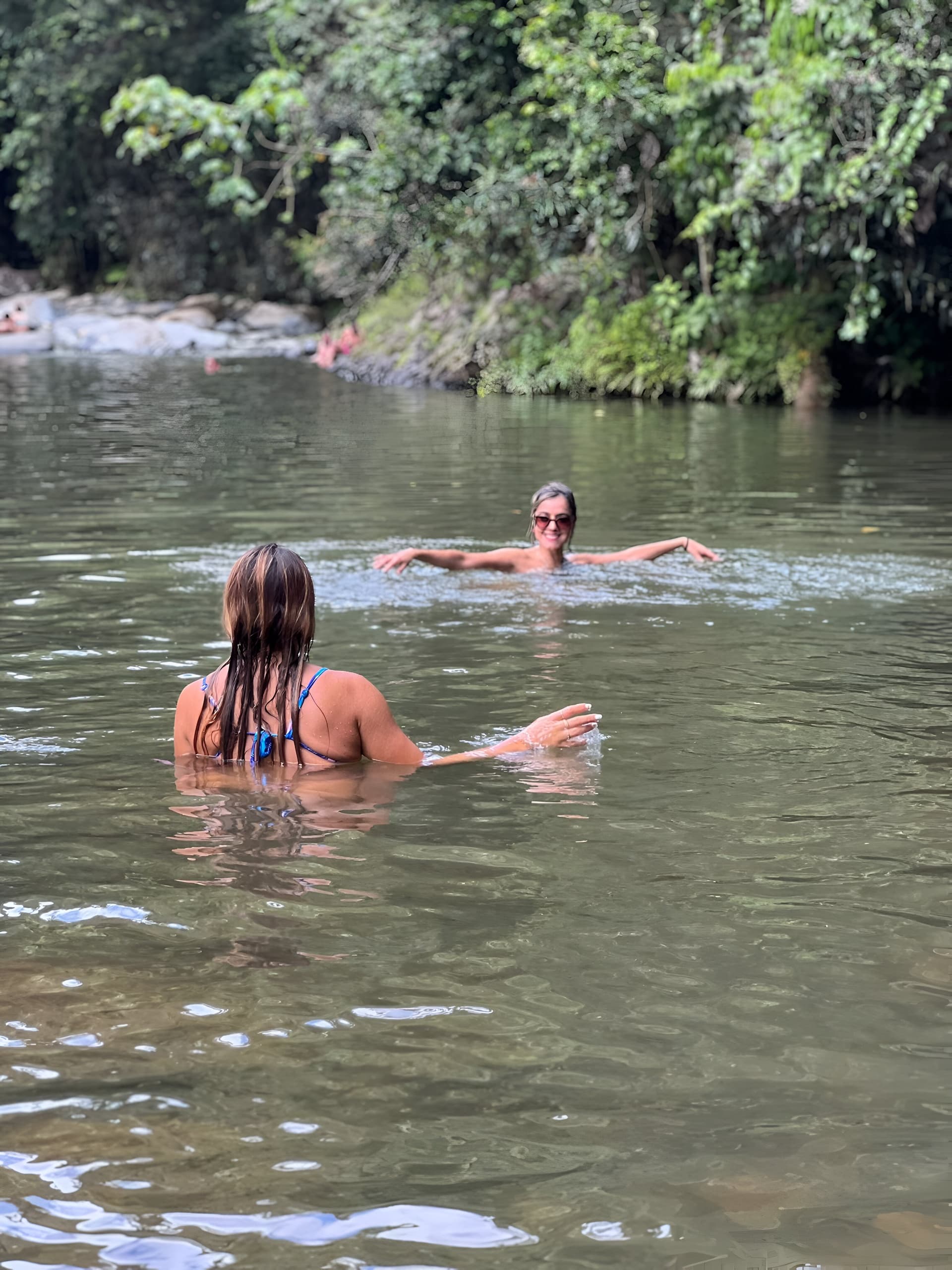 People swimming in a calm jungle river surrounded by rainforest