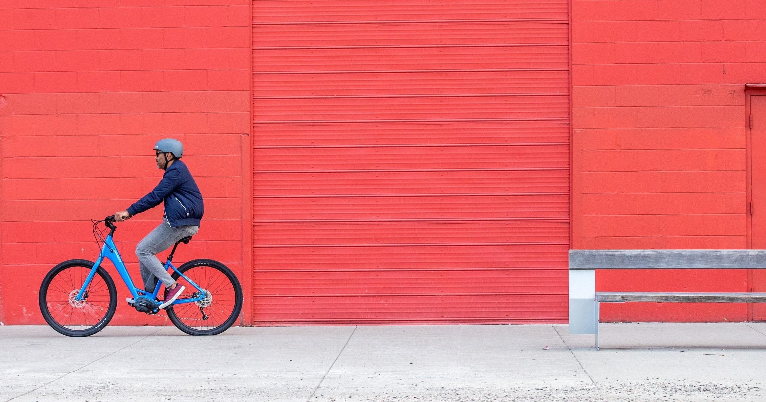 Cyclist riding past bright red wall on city sidewalk, casual ride