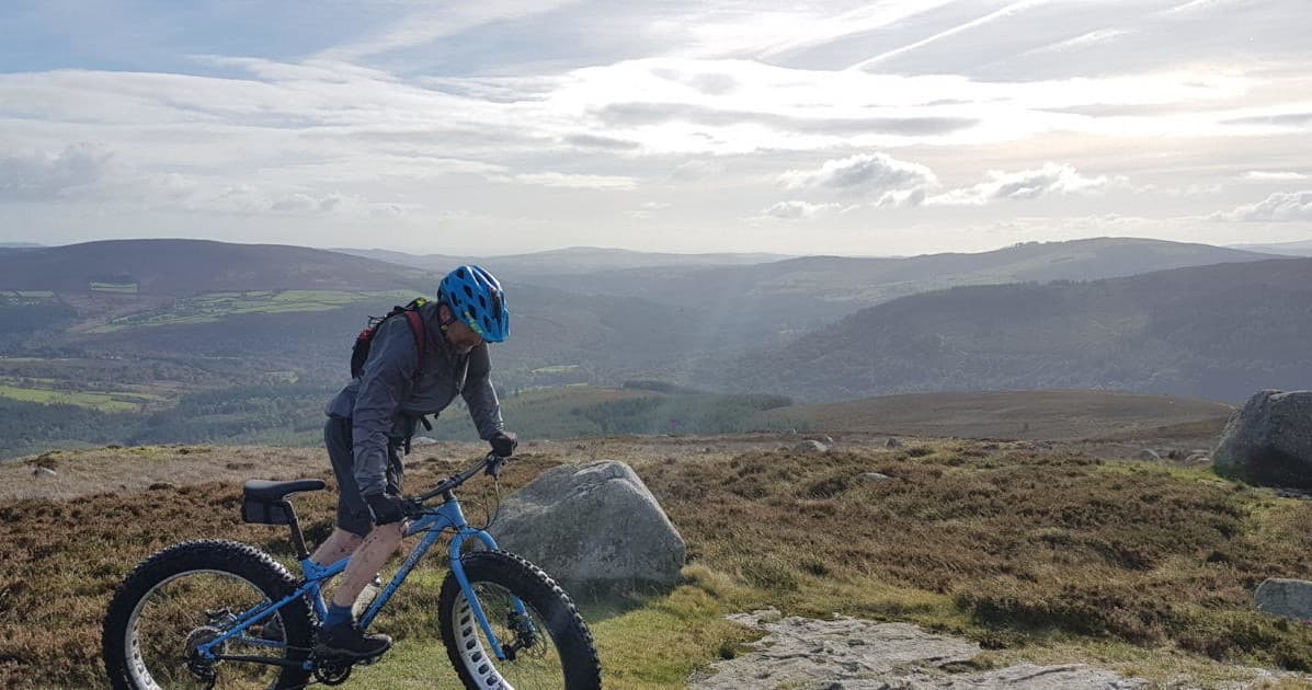 Fatbiker riding singletrack across windswept moorland vista