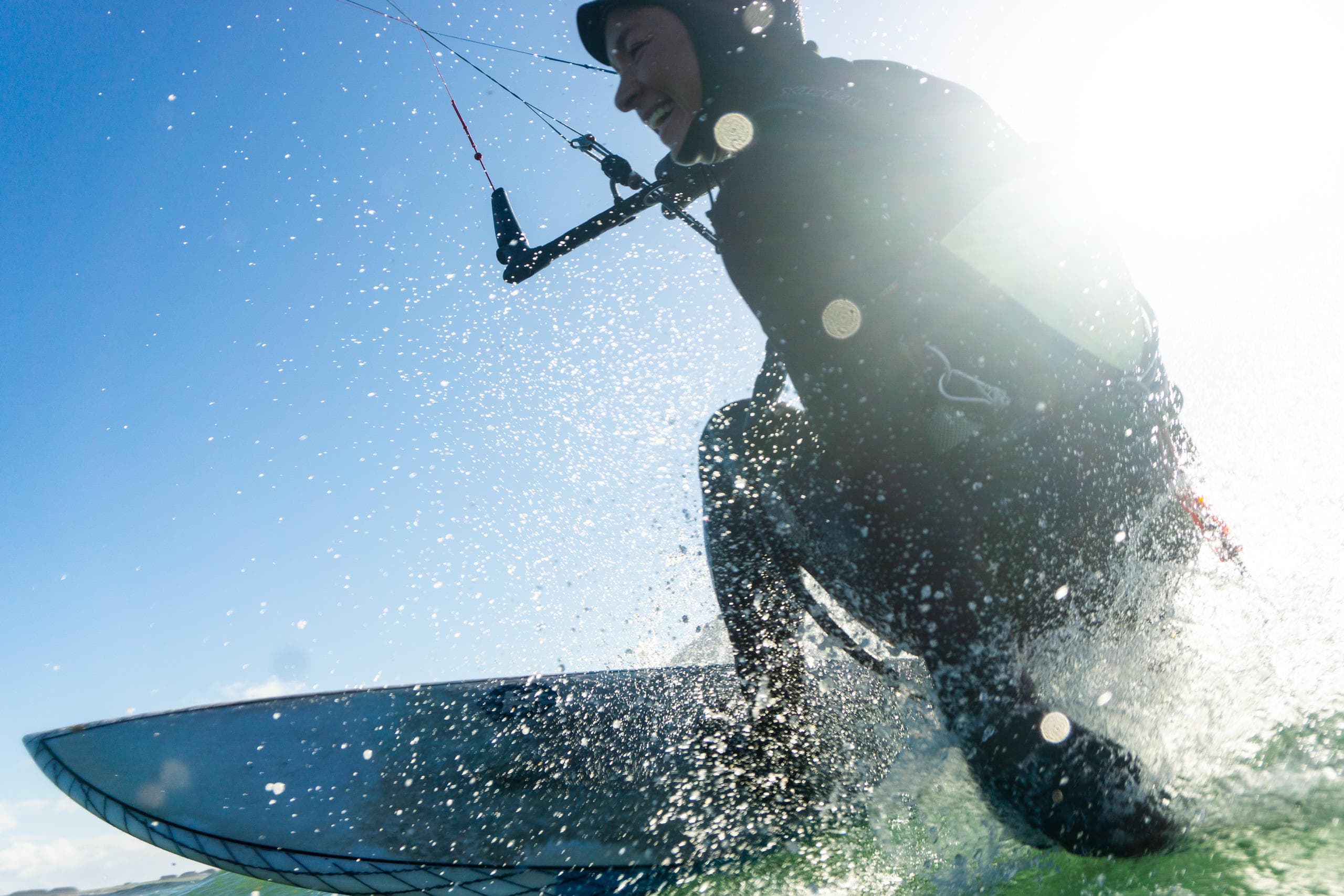 Kitesurfer carving across ocean with sun flare and clear sky