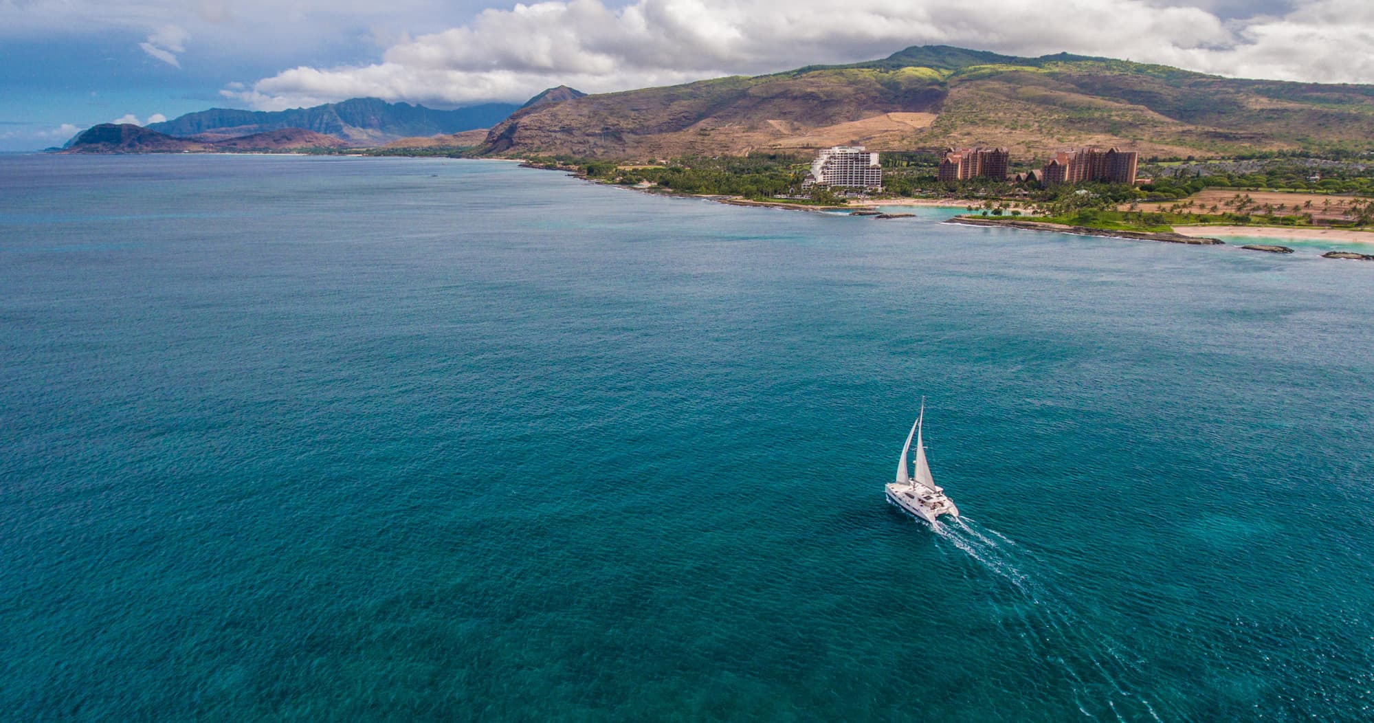 Single sailboat cruising coastal waters with island backdrop