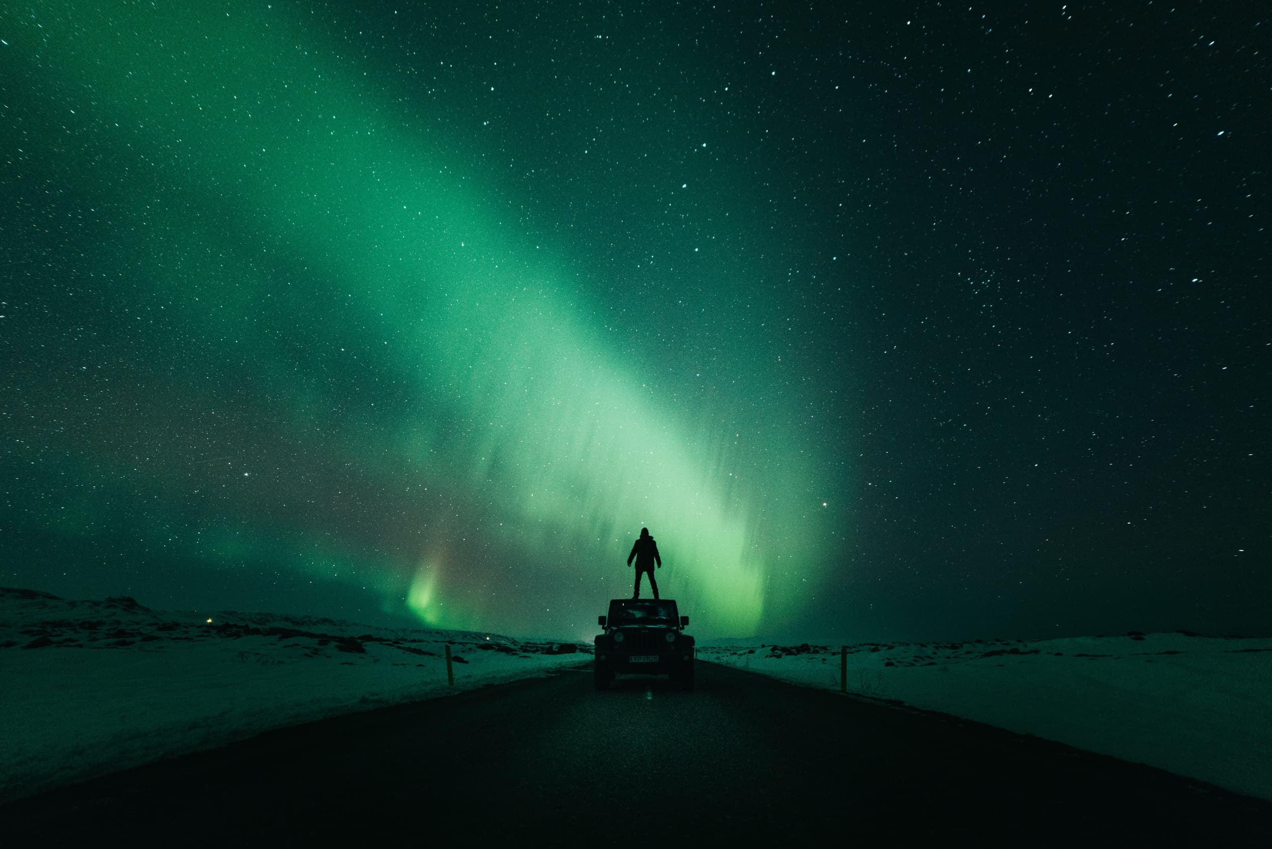 Aurora borealis over highway with vehicle silhouette at arctic night