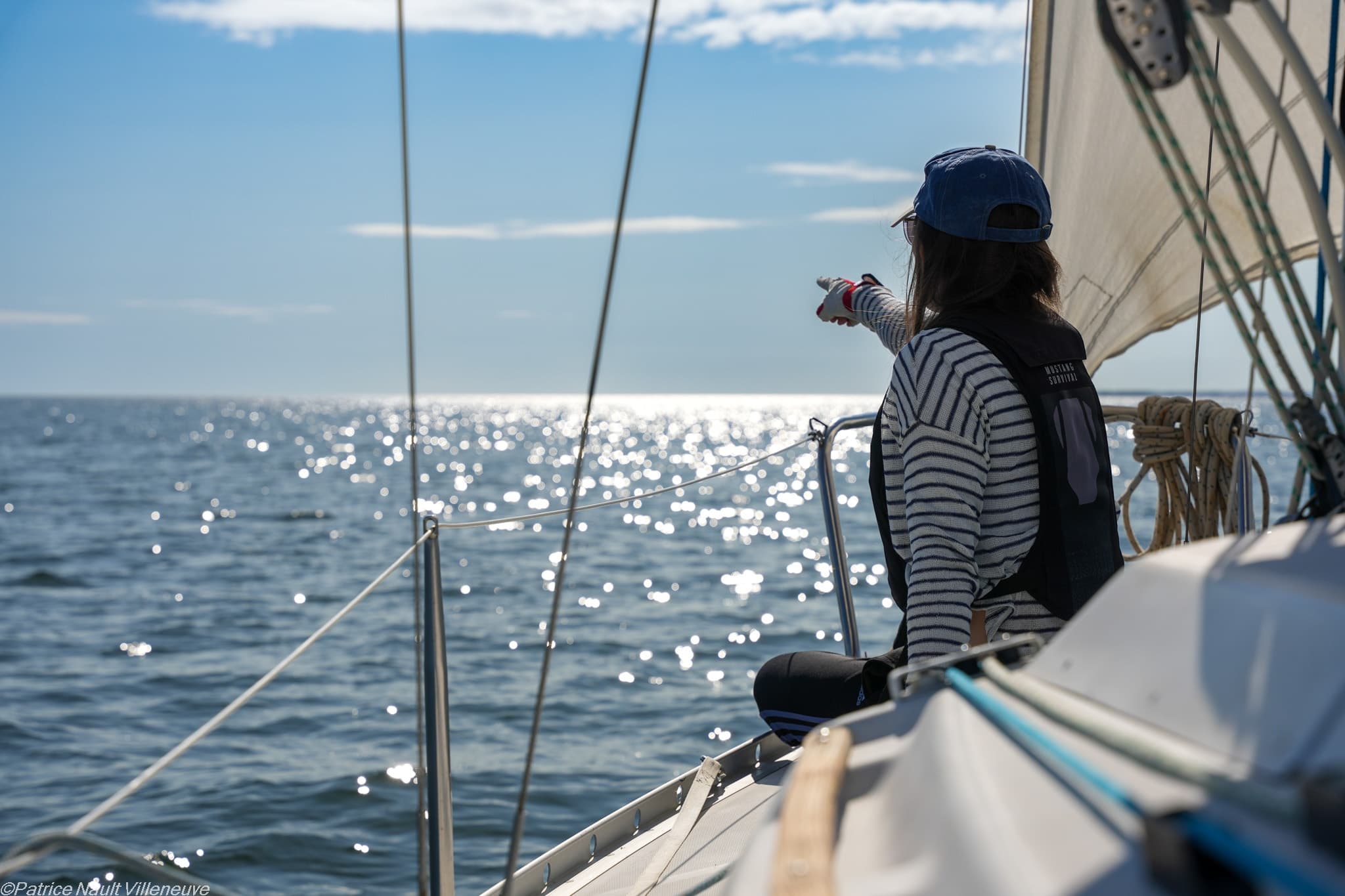 Sailor pointing toward the horizon aboard yacht at sea