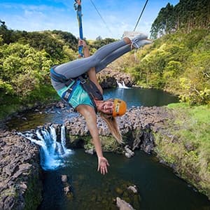 Adventurer performing upside down zipline trick over waterfall