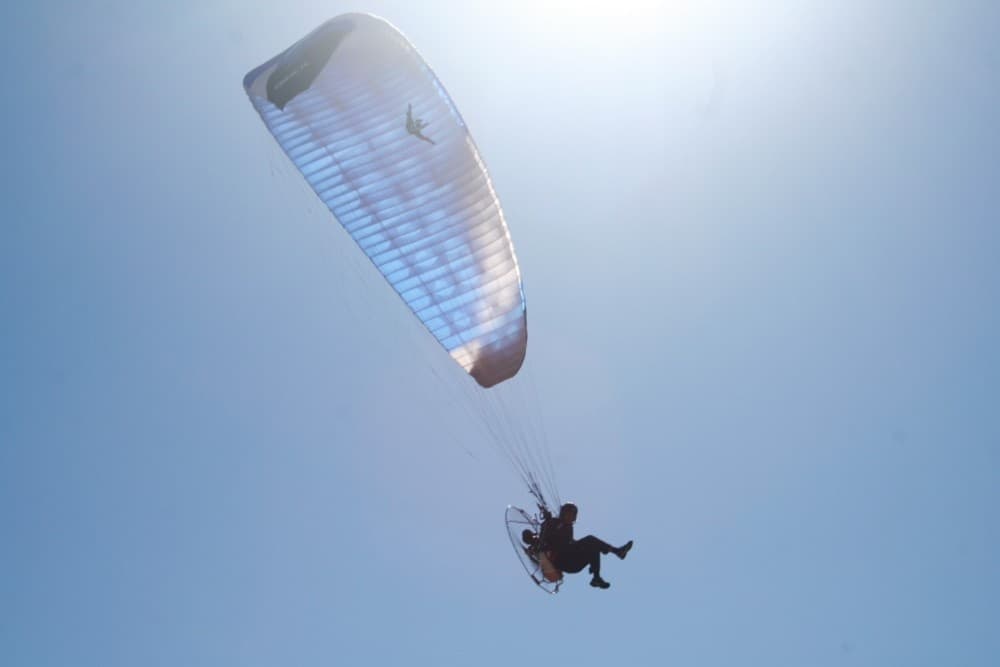 Paraglider pilot silhouetted against bright blue sky near Madrid
