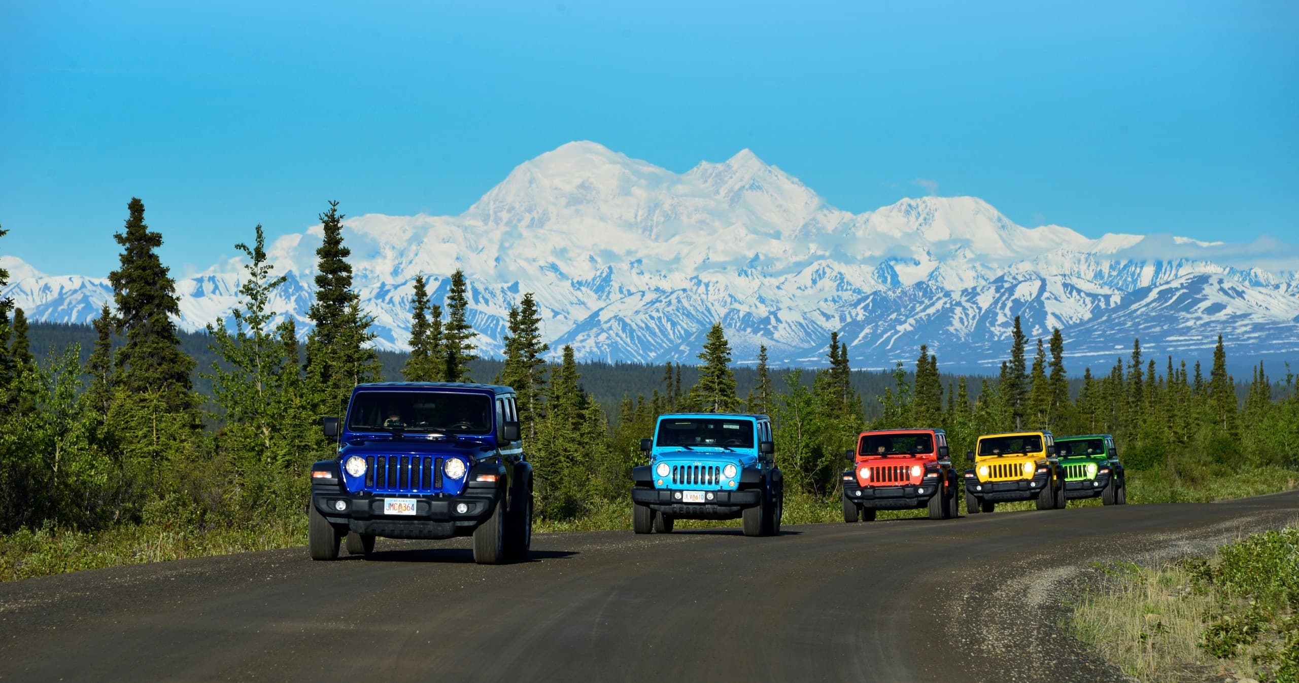 Four colorful Jeeps driving near Denali with mountain backdrop