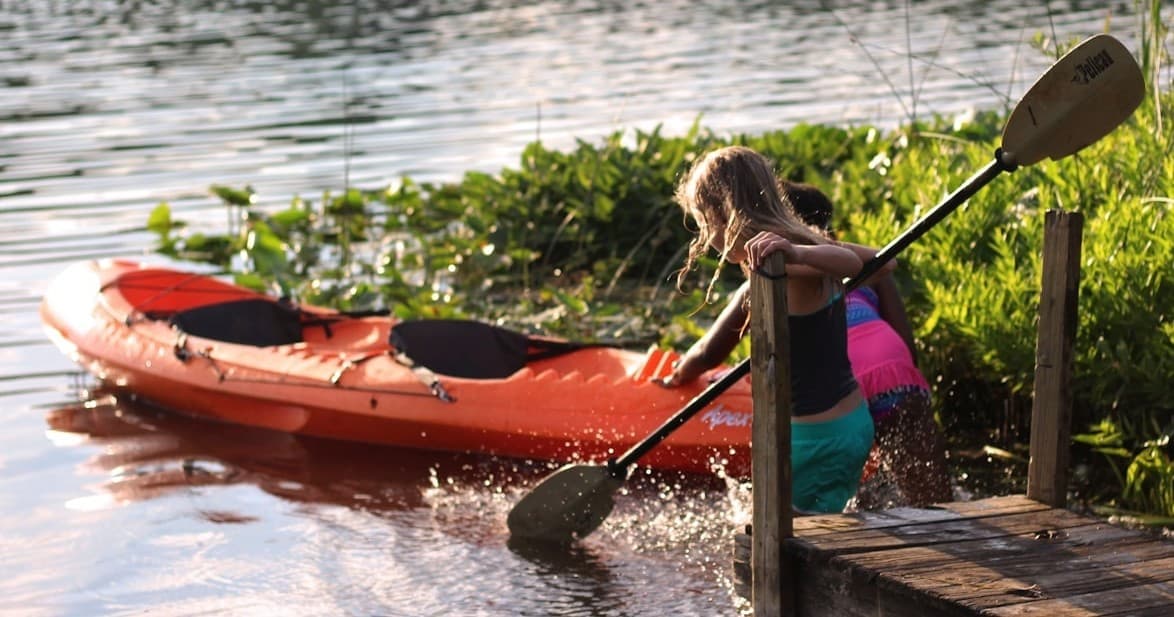 Woman launching orange kayak from lakeside dock at sunset