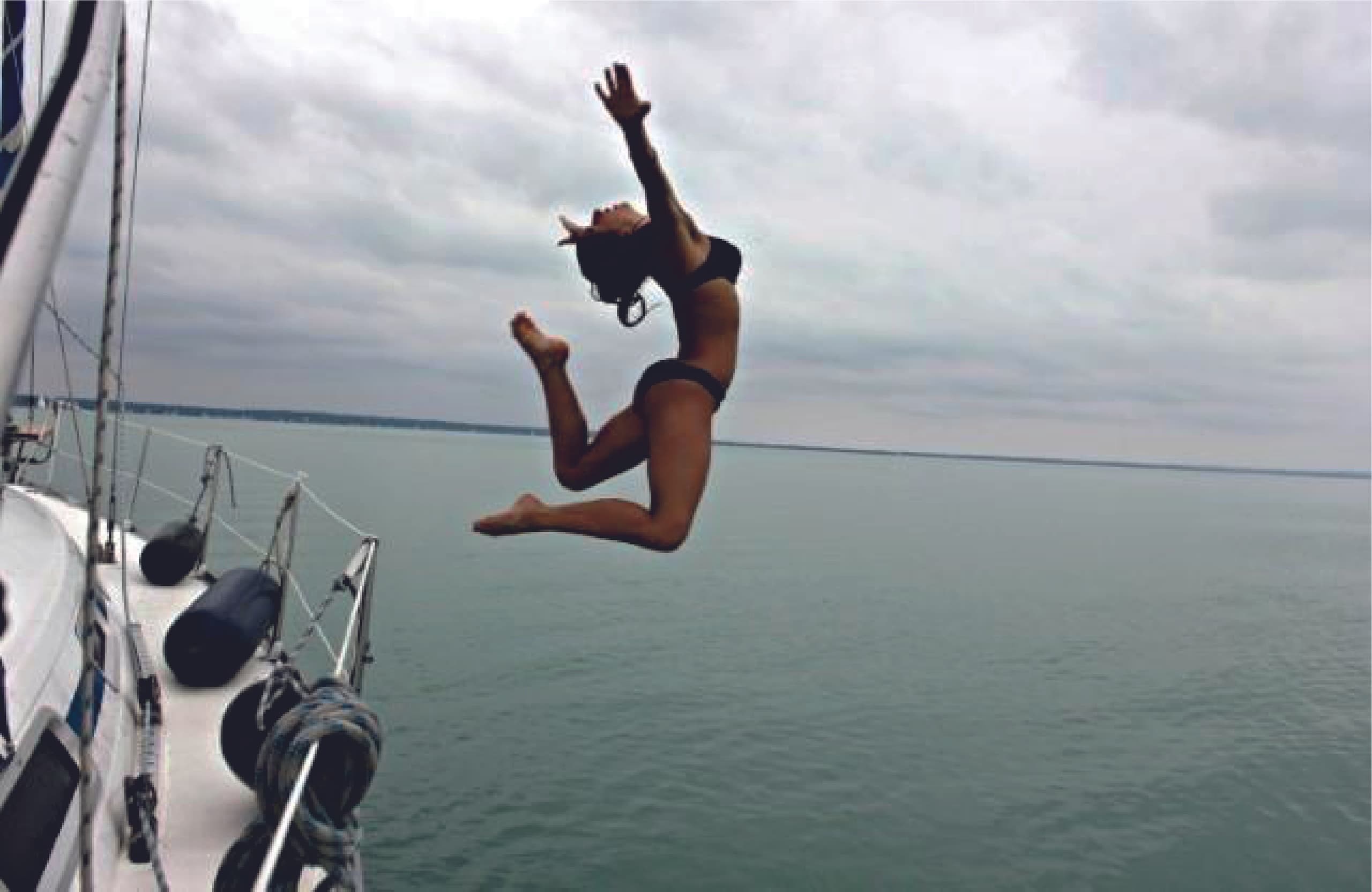 Person mid-air jump off sailboat into calm open ocean