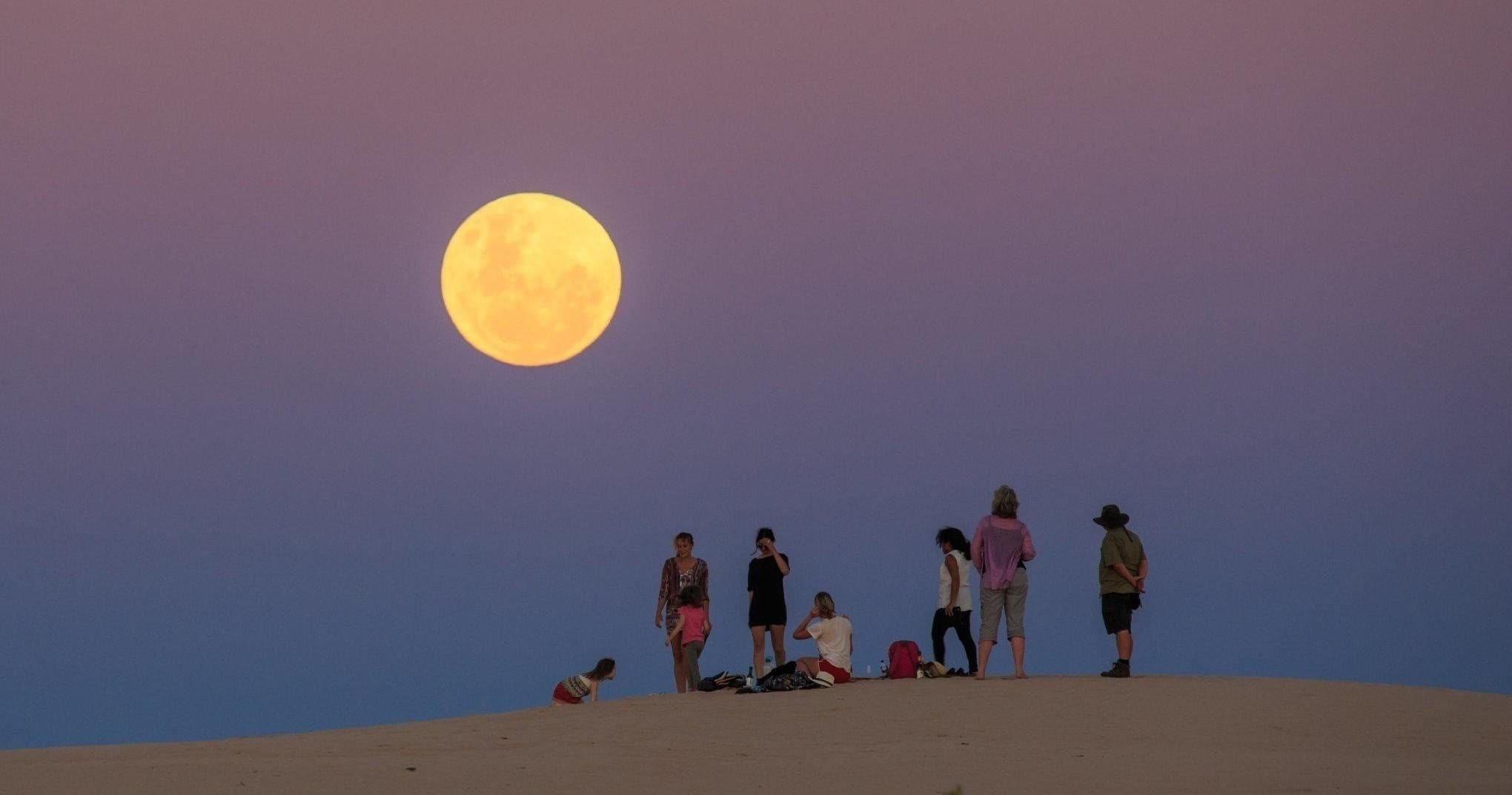 Full moon rising over sand dune with small tour group