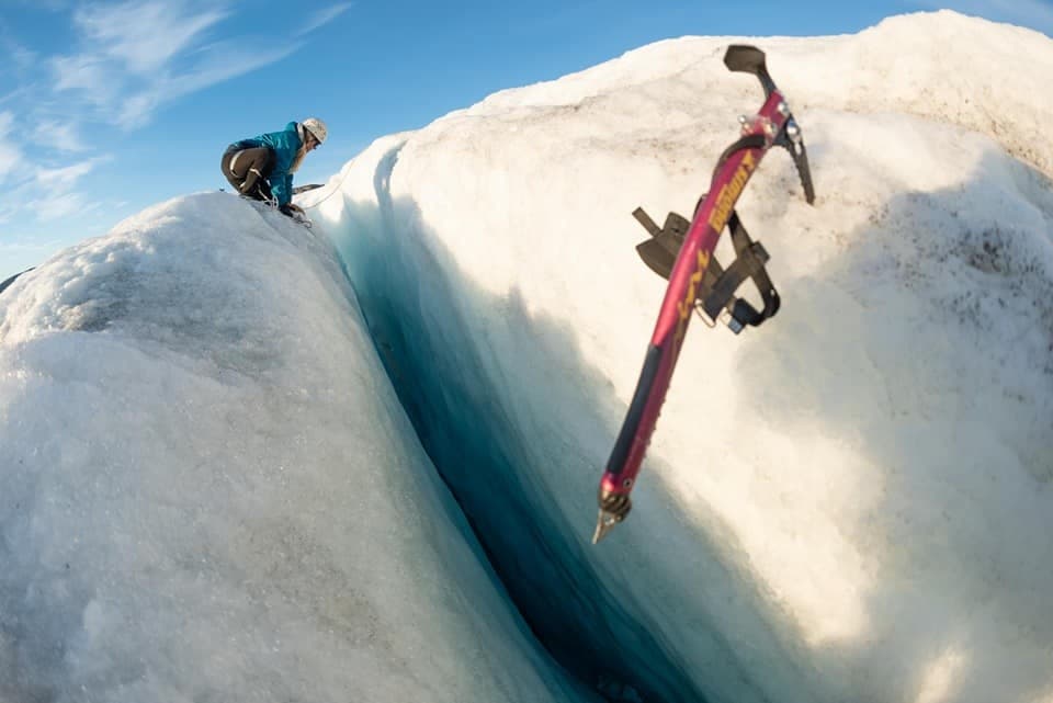 Ice climber dropping axe over crevasse, glacier adventure shot