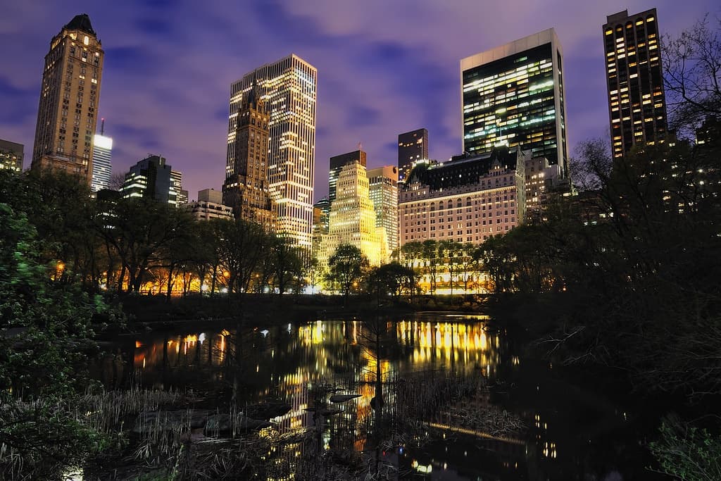 Night skyline over Central Park pond reflecting illuminated towers