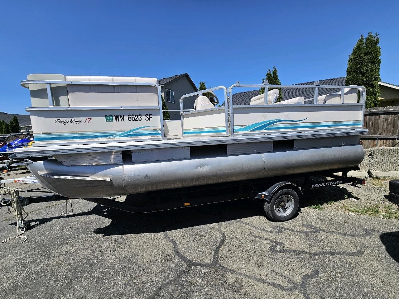 White pontoon boat on trailer in a residential parking lot