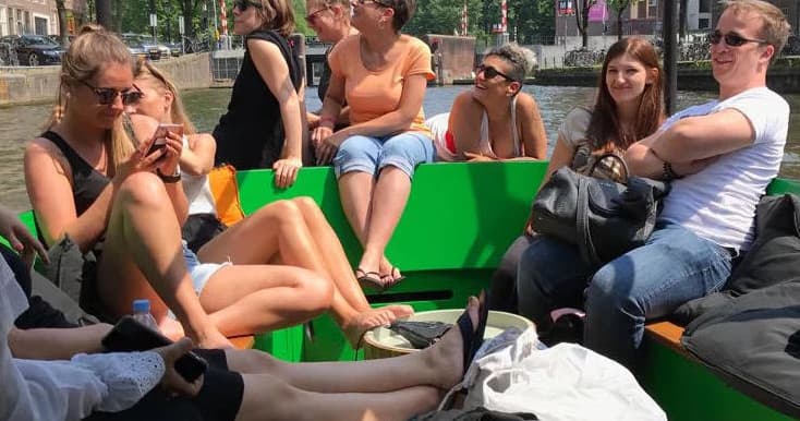 Group relaxing on open green-deck boat riding Amsterdam canal