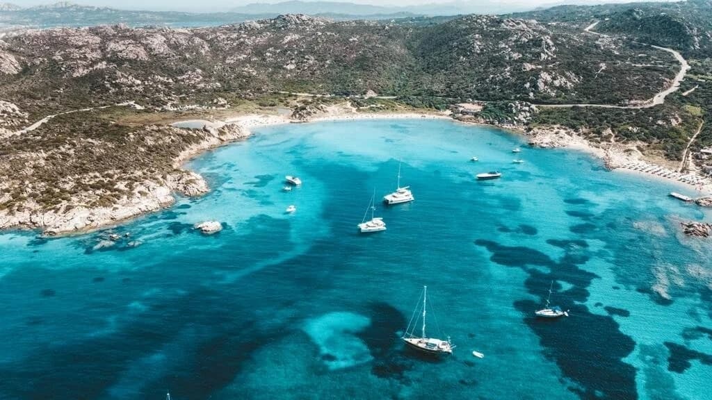 Sailboats anchored in a turquoise coastal bay near rocky island shores