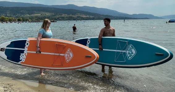 Shoreline surfers holding paddleboards with mountain backdrop