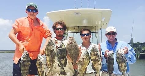 Group of anglers holding large flounder and saltwater catches on boat