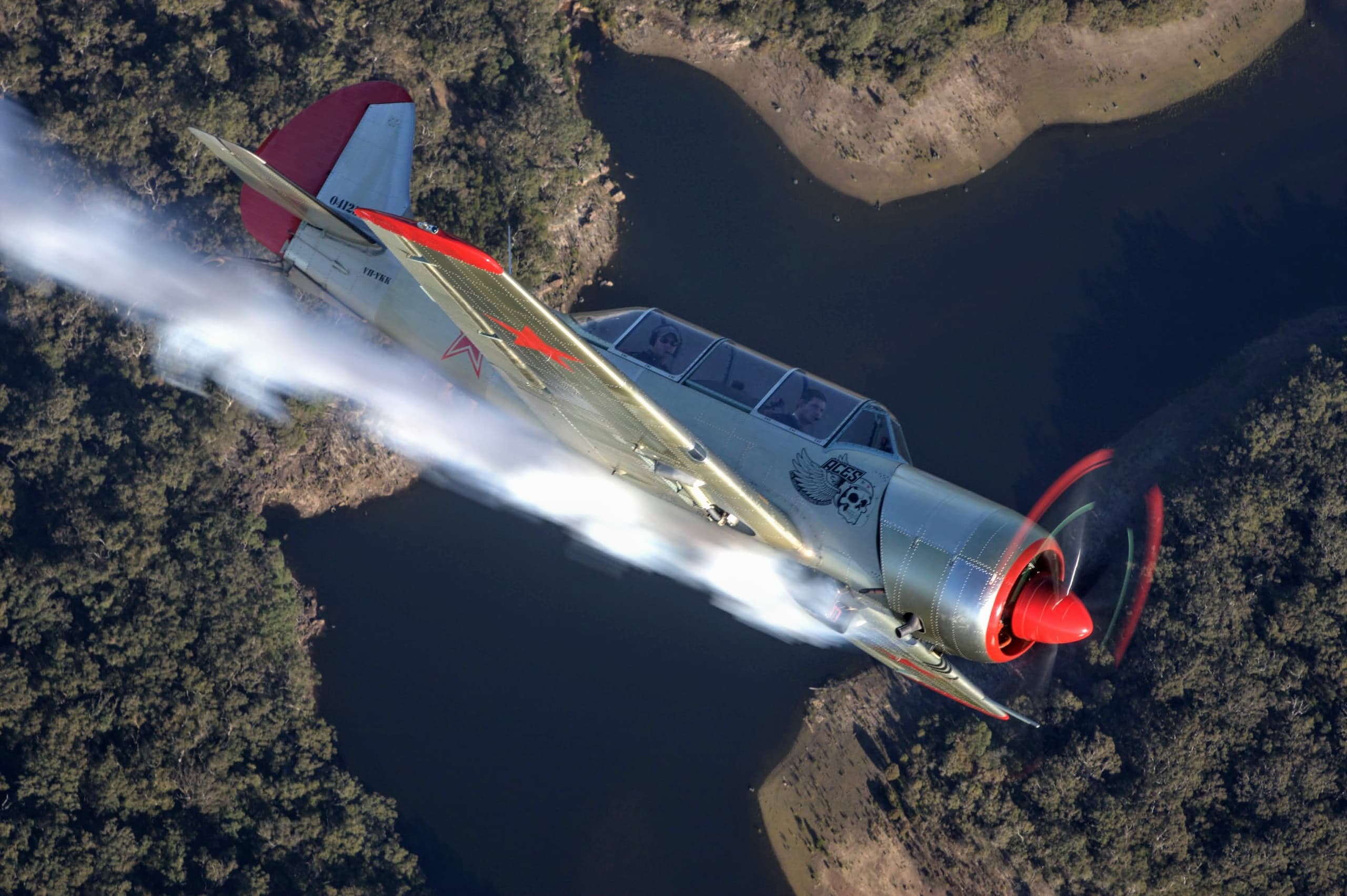 Aerobatic warplane banking over river and woodland scenery