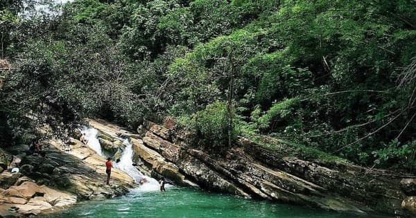 Person hiking by tropical river and rocky waterfall in rainforest