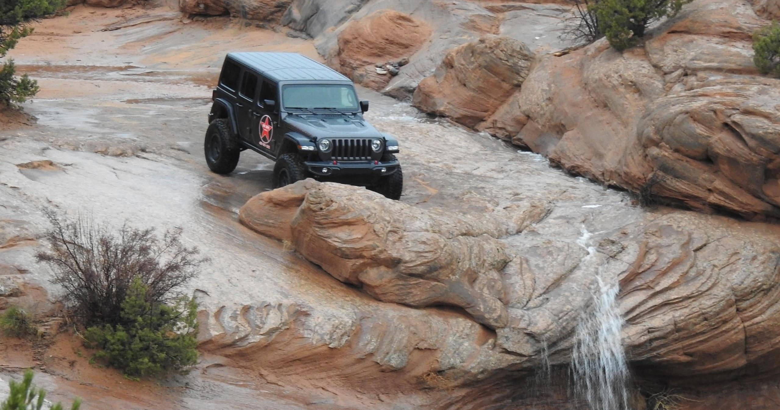 Jeep descending slickrock near canyon waterfall on off-road tour