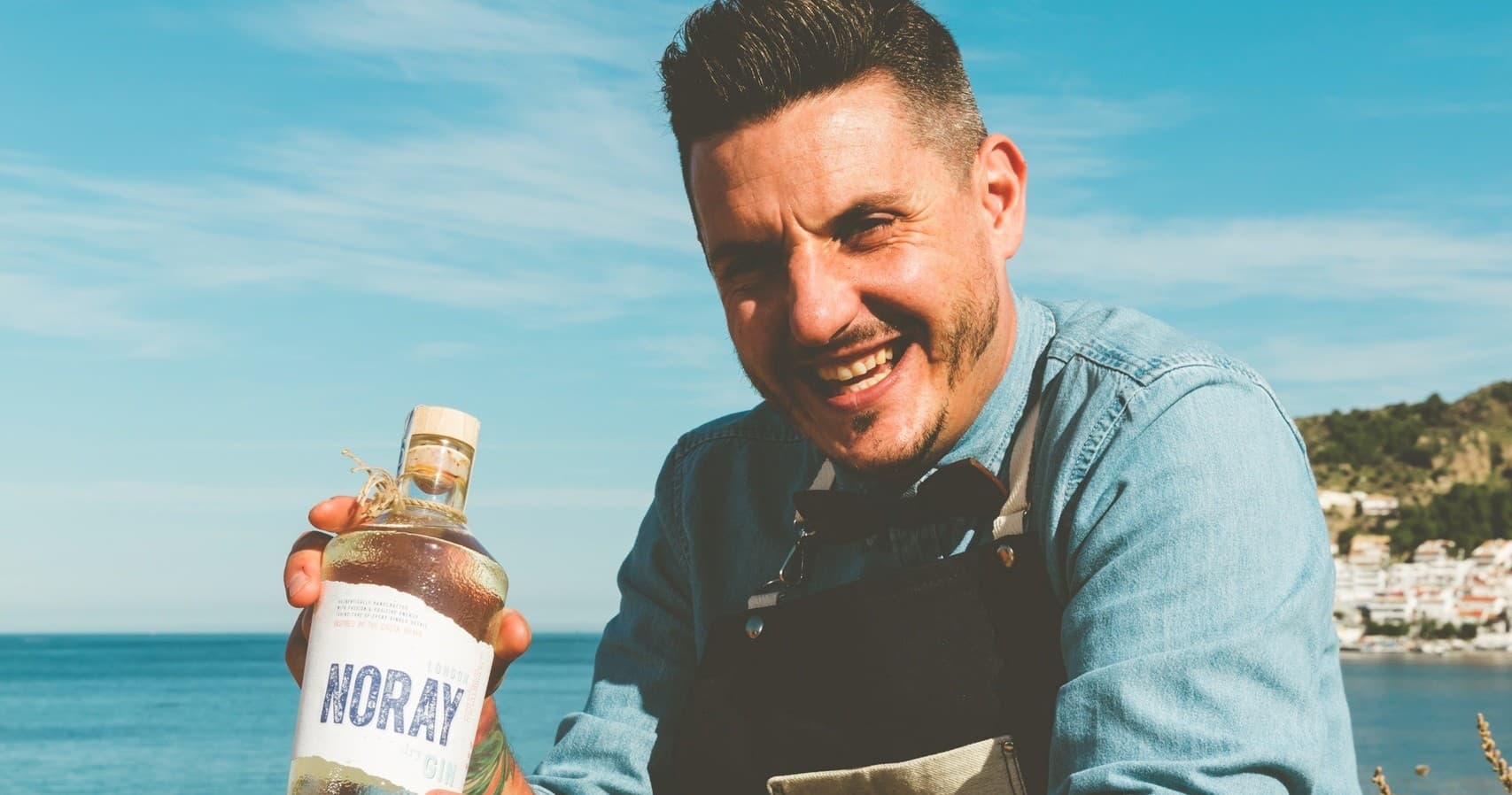 Smiling host holding craft spirit bottle on coastal boat