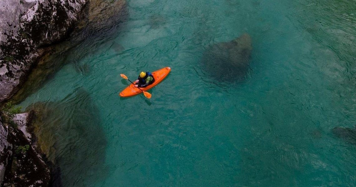 Solo kayaker paddling near coastal cliffs in turquoise bay