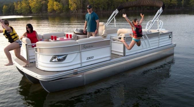 Friends jumping from pontoon boat into lake during summer outing