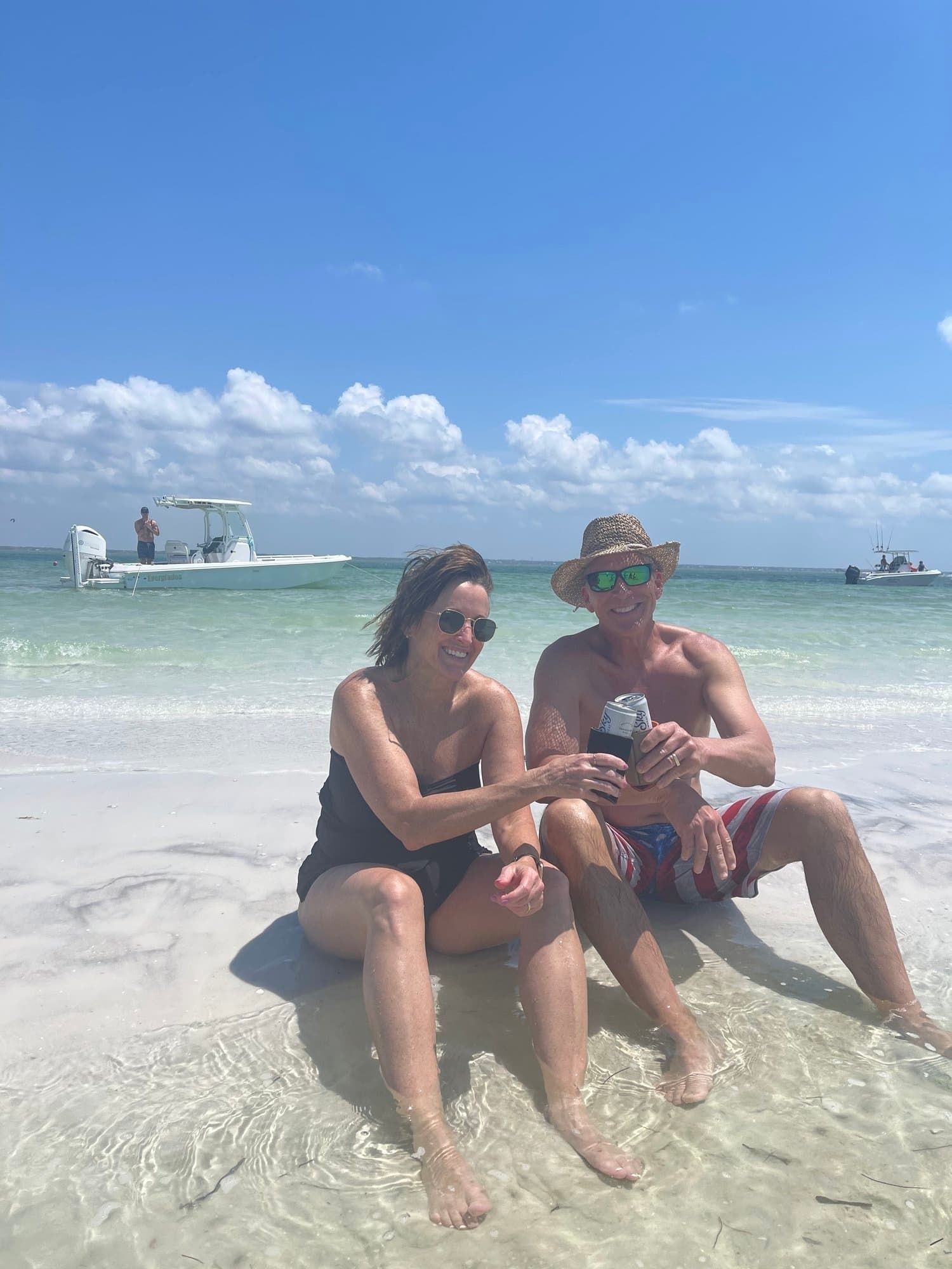 Couple relaxing on Gulf beach in shallow water with boat