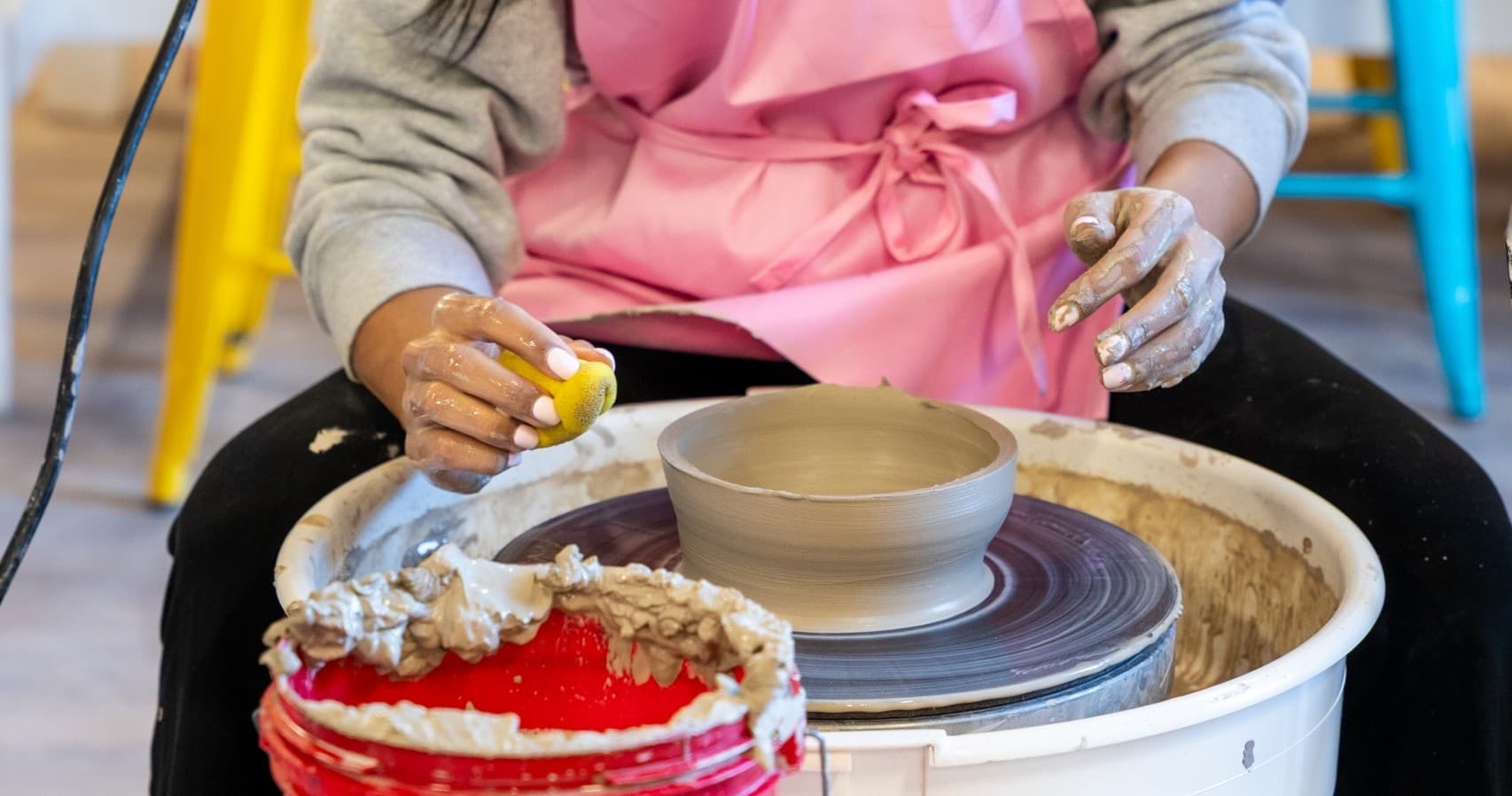 Instructor guiding student at pottery wheel in studio workshop