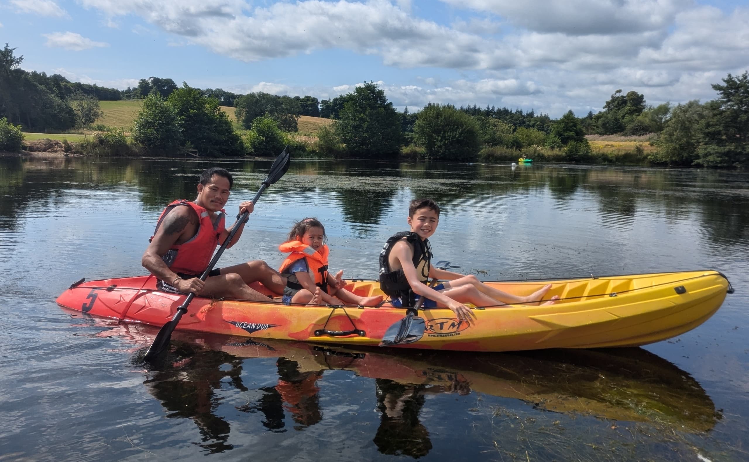 Two adults and child kayaking a scenic river inlet on a sunny day