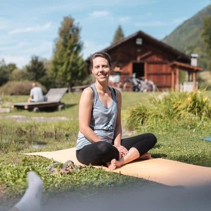 Woman practicing outdoor yoga on mat near mountain cabin