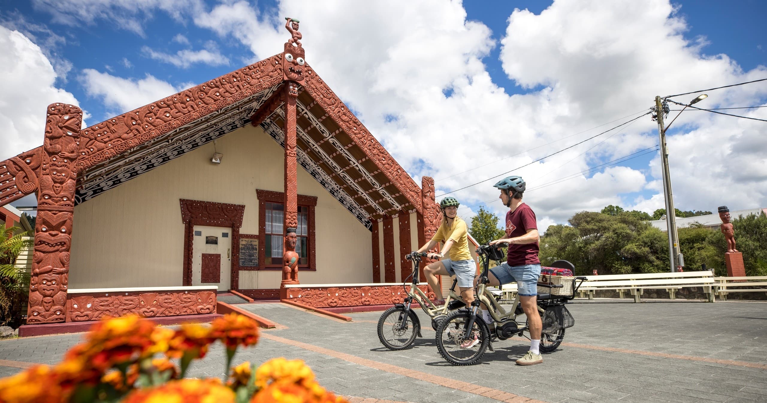 Cyclists outside carved Maori meeting house, cultural village scene