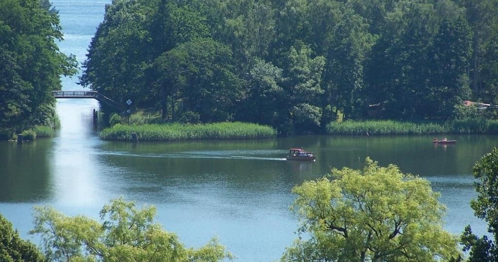 Forested lake cruise with distant boat on tranquil water