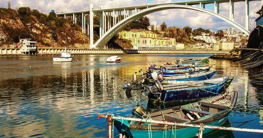 Colorful fishing boats on river under arched bridge at sunset