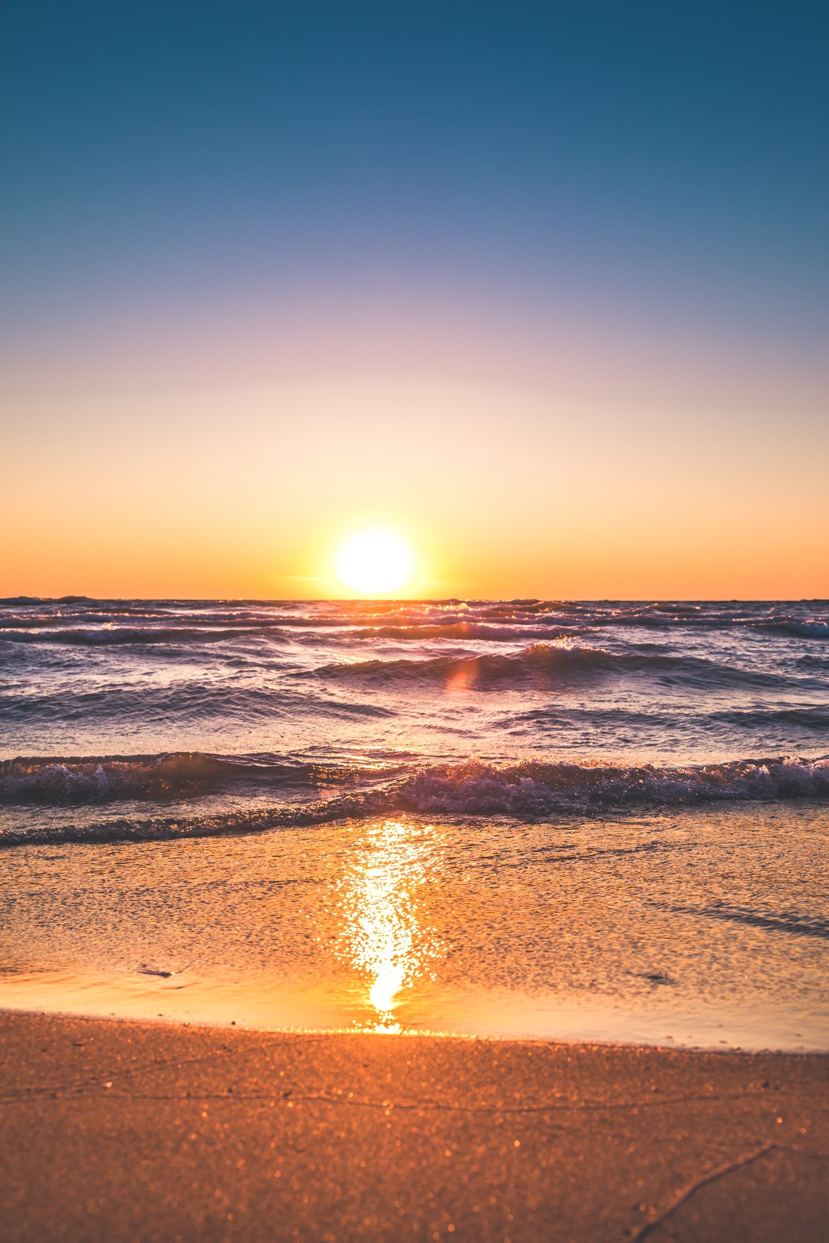 Sunset over sandy beach with gentle waves, tranquil shoreline view