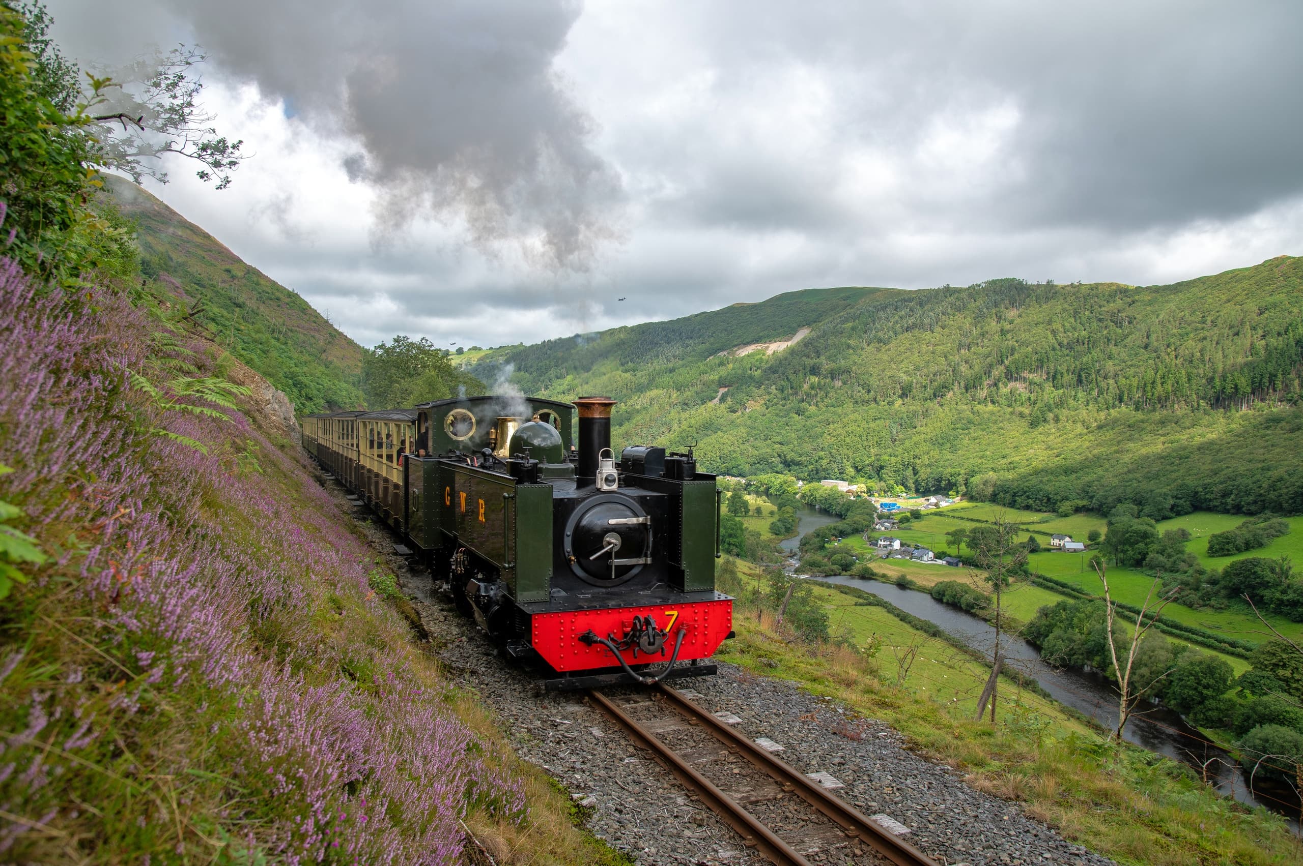 Steam train climbing green Welsh hills through valley scenery