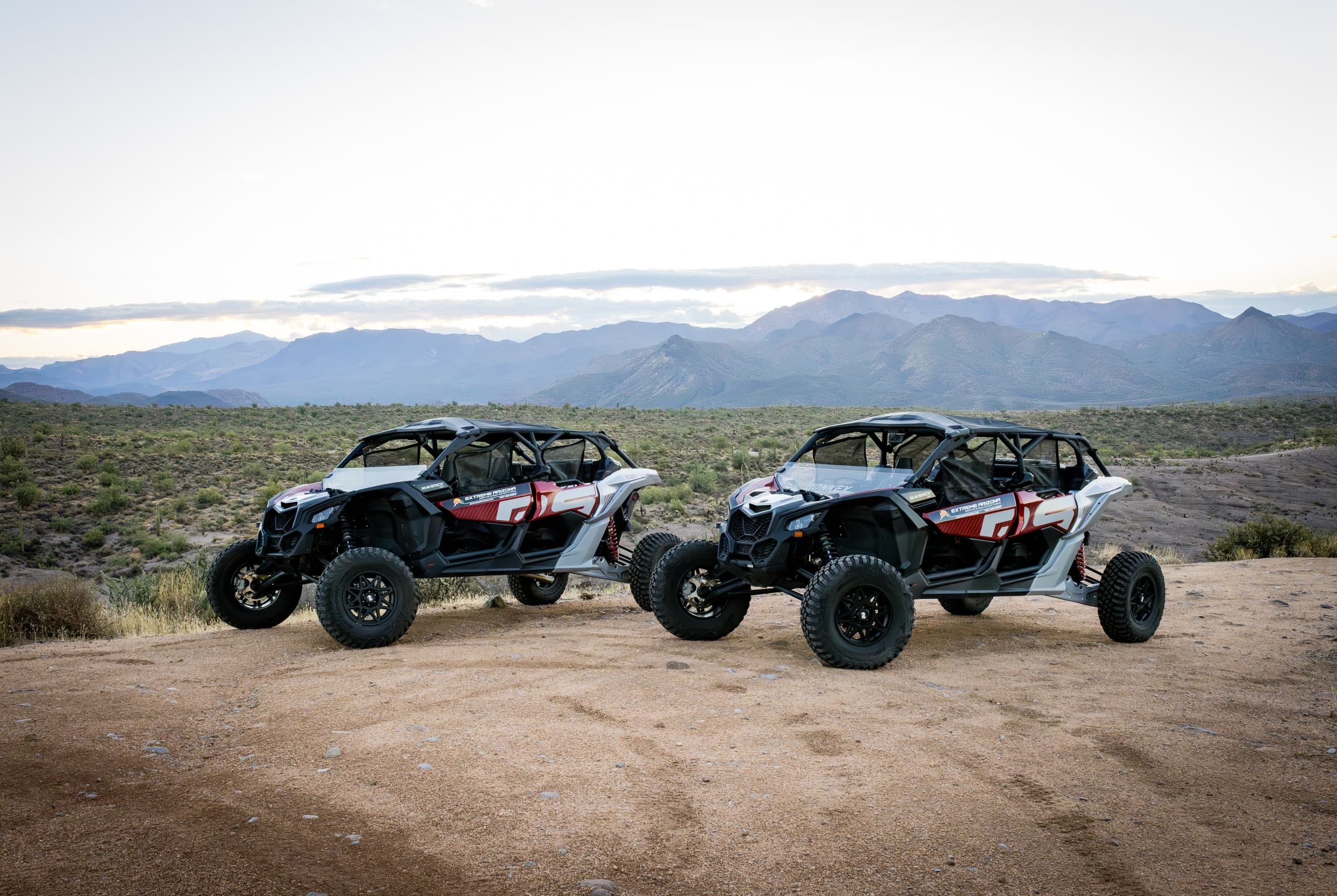 Two UTVs parked on desert trail with mountains at sunset